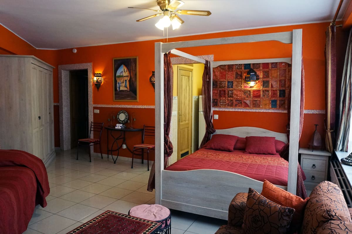 Una habitación con cama con dosel, un escritorio con silla, una mesita y un ventanal con cortinas.