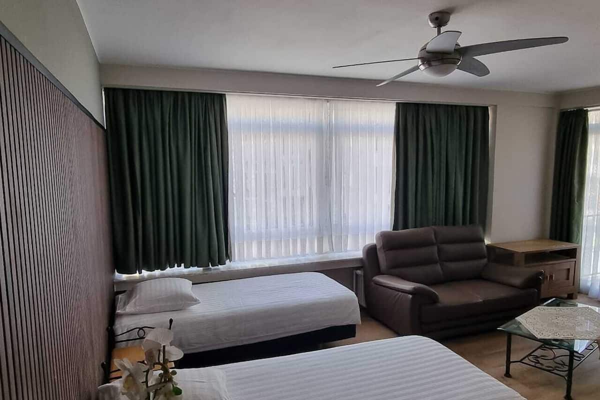 Habitación de hotel con dos camas individuales, un sofá, una mesita y un ventilador de techo.