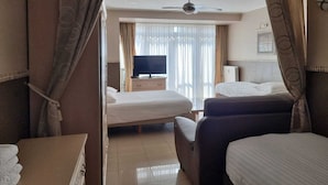 Une chambre d’hôtel avec deux lits, une télévision, un ventilateur de plafond et une fenêtre avec des rideaux.