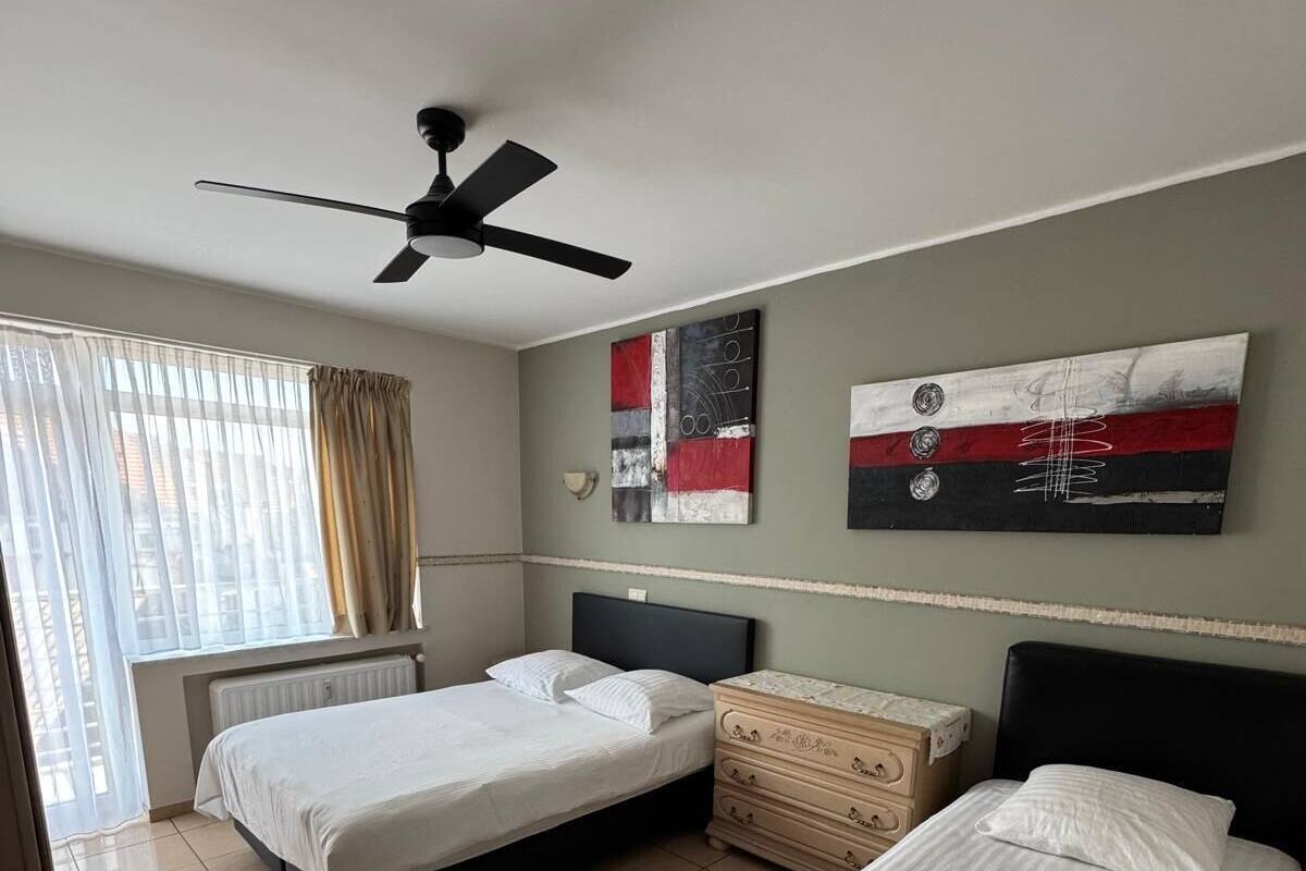 Habitación de hotel con dos camas, un ventilador de techo, un aparador y obras de arte en la pared.