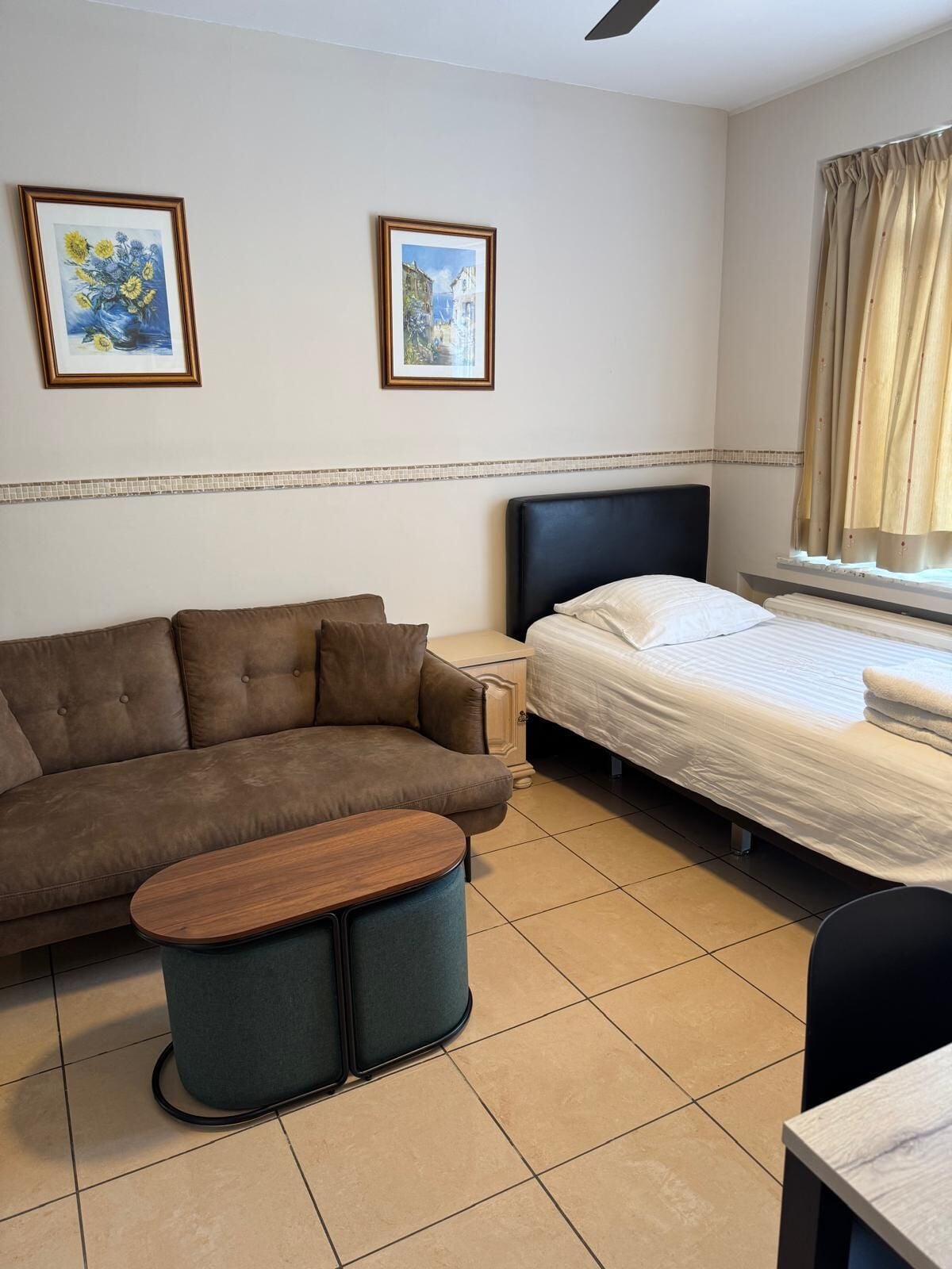 Una habitación de hotel con un sofá marrón, una cama con ropa blanca, una mesita redonda y dos cuadros en la pared.