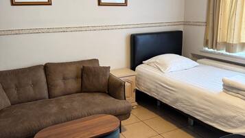 Una habitación de hotel con un sofá marrón, una cama con ropa blanca, una mesita redonda y dos cuadros en la pared.