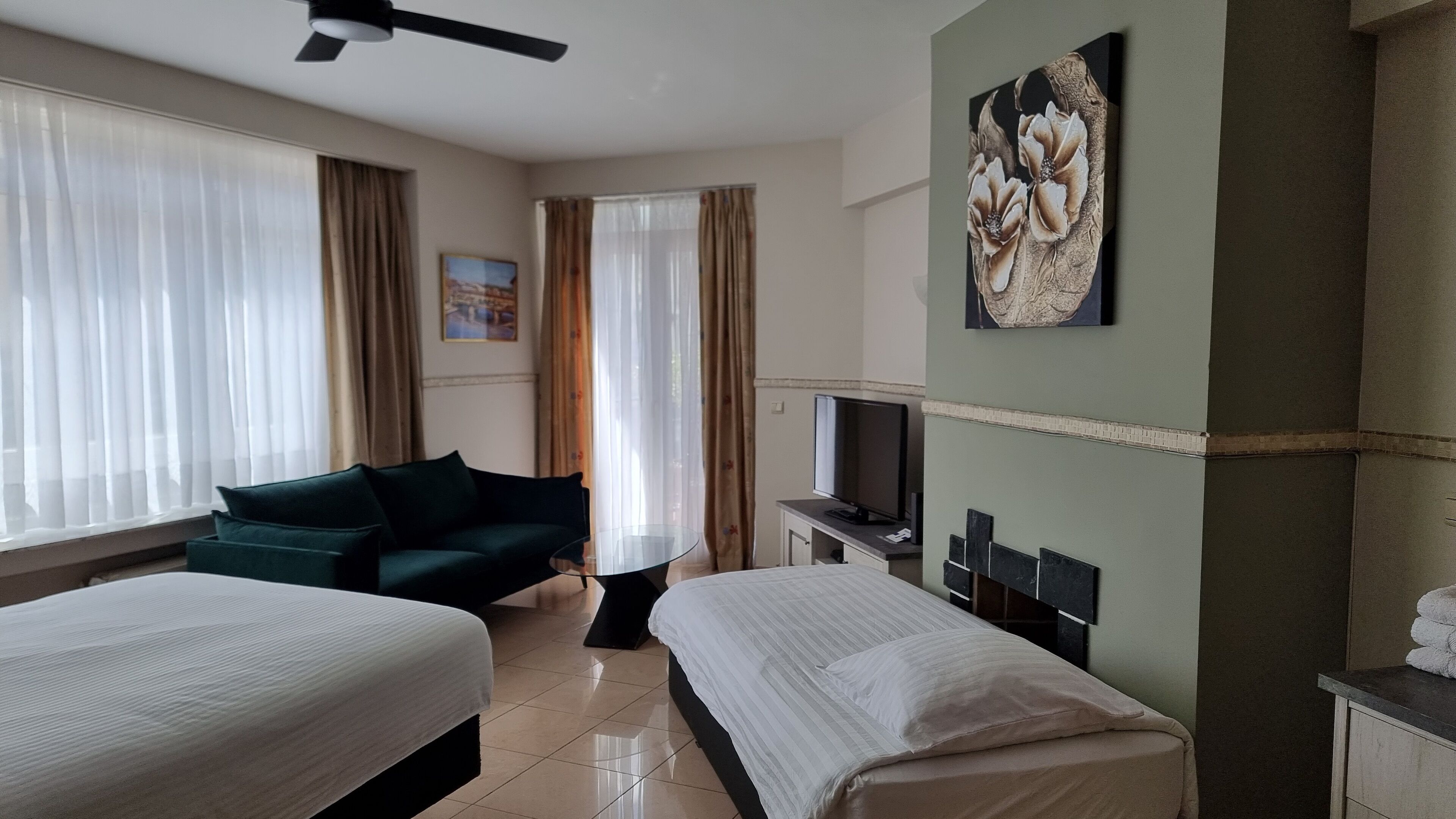 Ein Hotelzimmer mit zwei Betten, einem Schlafsofa, einem Fernseher und einem Bild an der Wand.