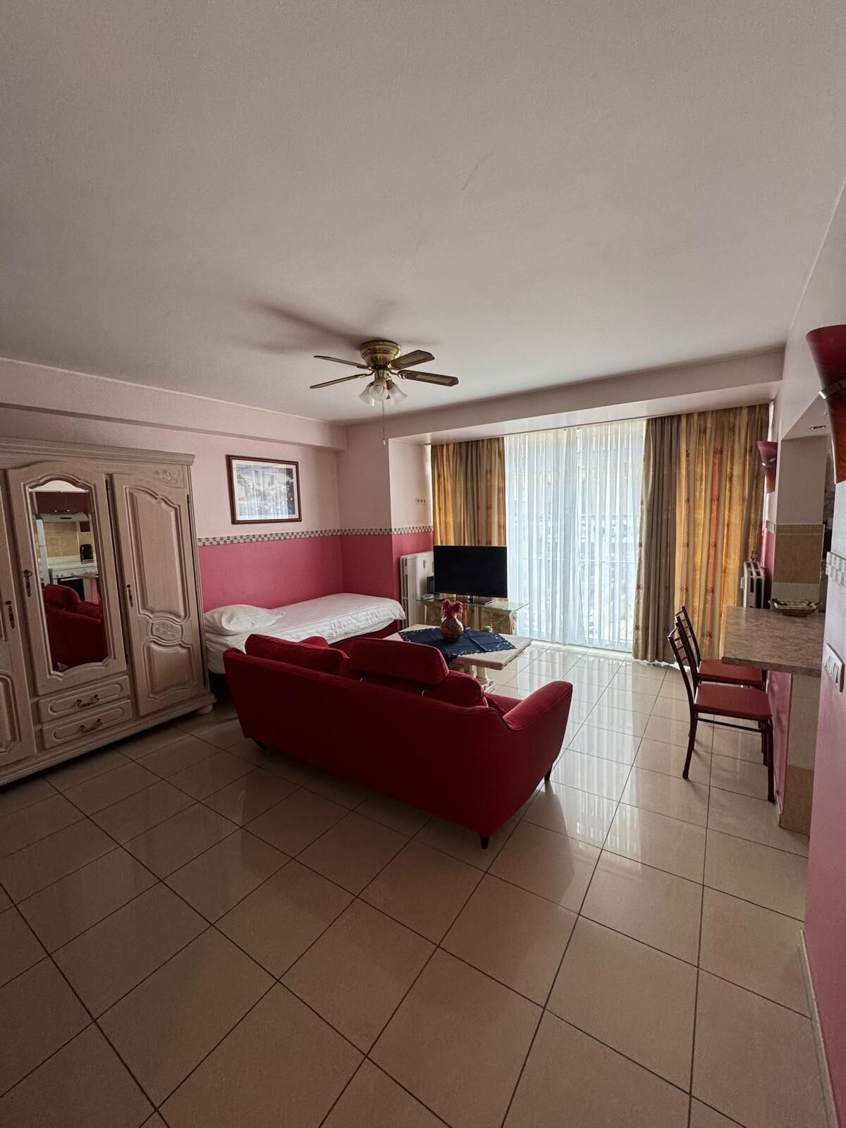 Une chambre d’hôtel avec un lit, un canapé rouge, une télévision, un bureau et une armoire.