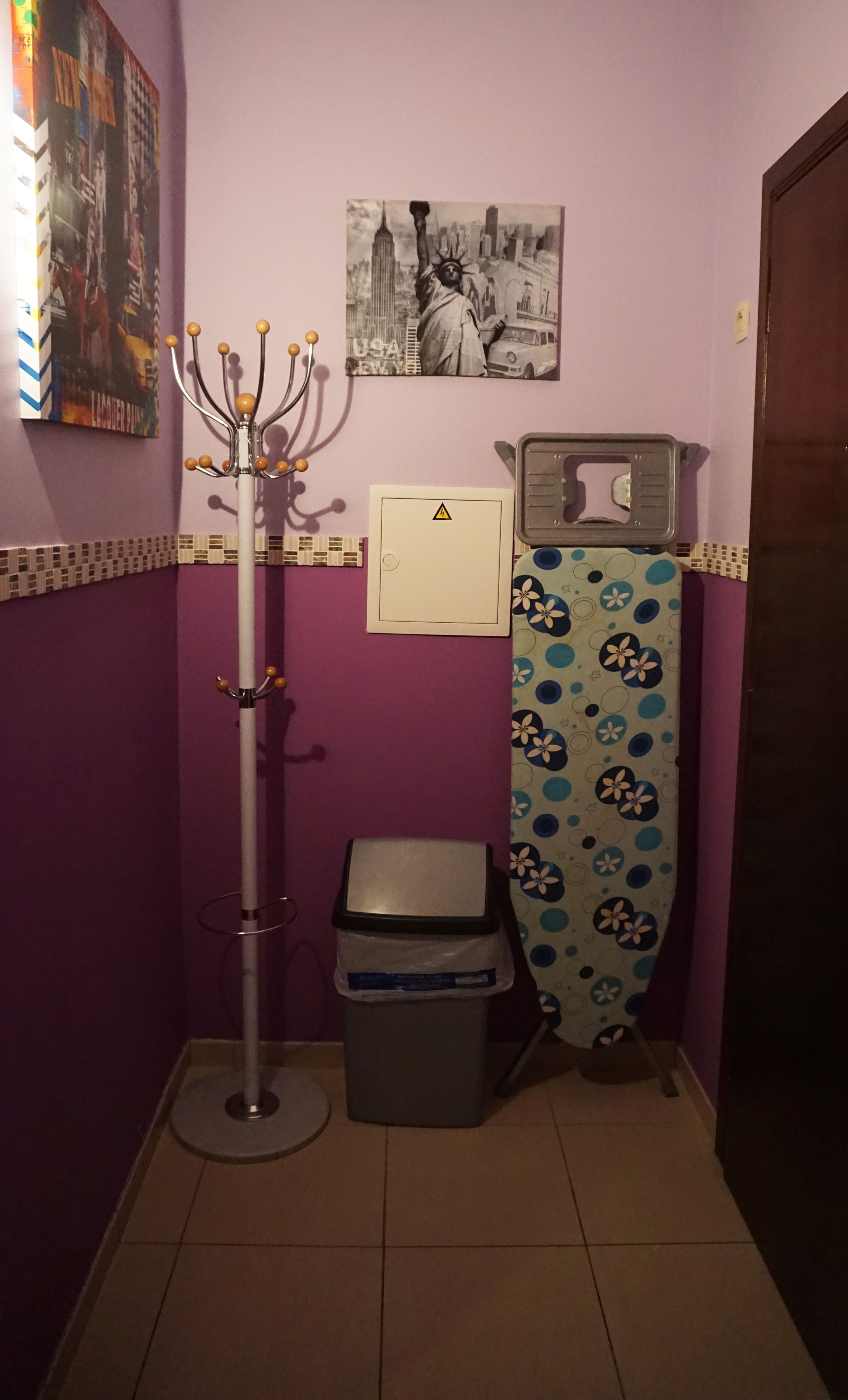 Ein Badezimmer mit Mülleimer, Kleiderhaken, einem Bild an der Wand und einer Duschvorhang.