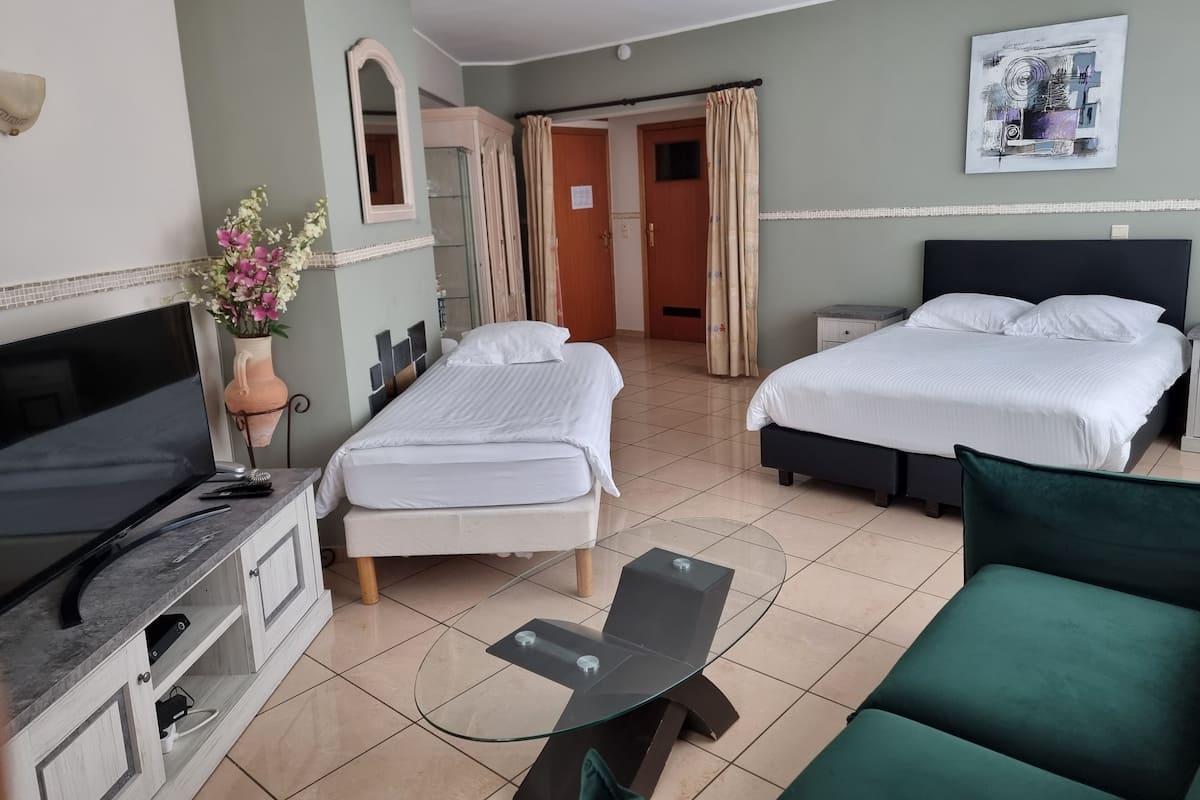 Habitación de hotel con dos camas, televisión, escritorio con computadora, sofá verde y ventilador de techo.
