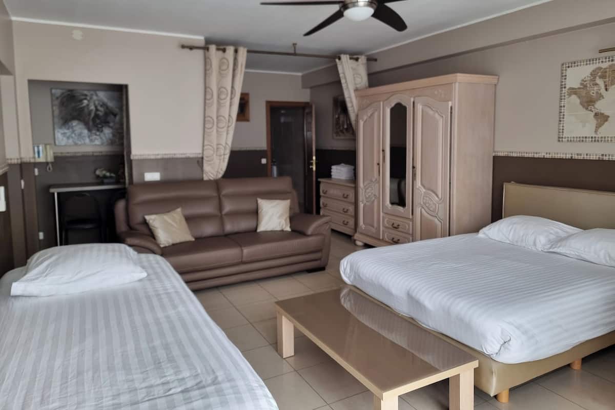 Una habitación de hotel con dos camas, un sofá, un escritorio, un armario y un ventilador de techo.