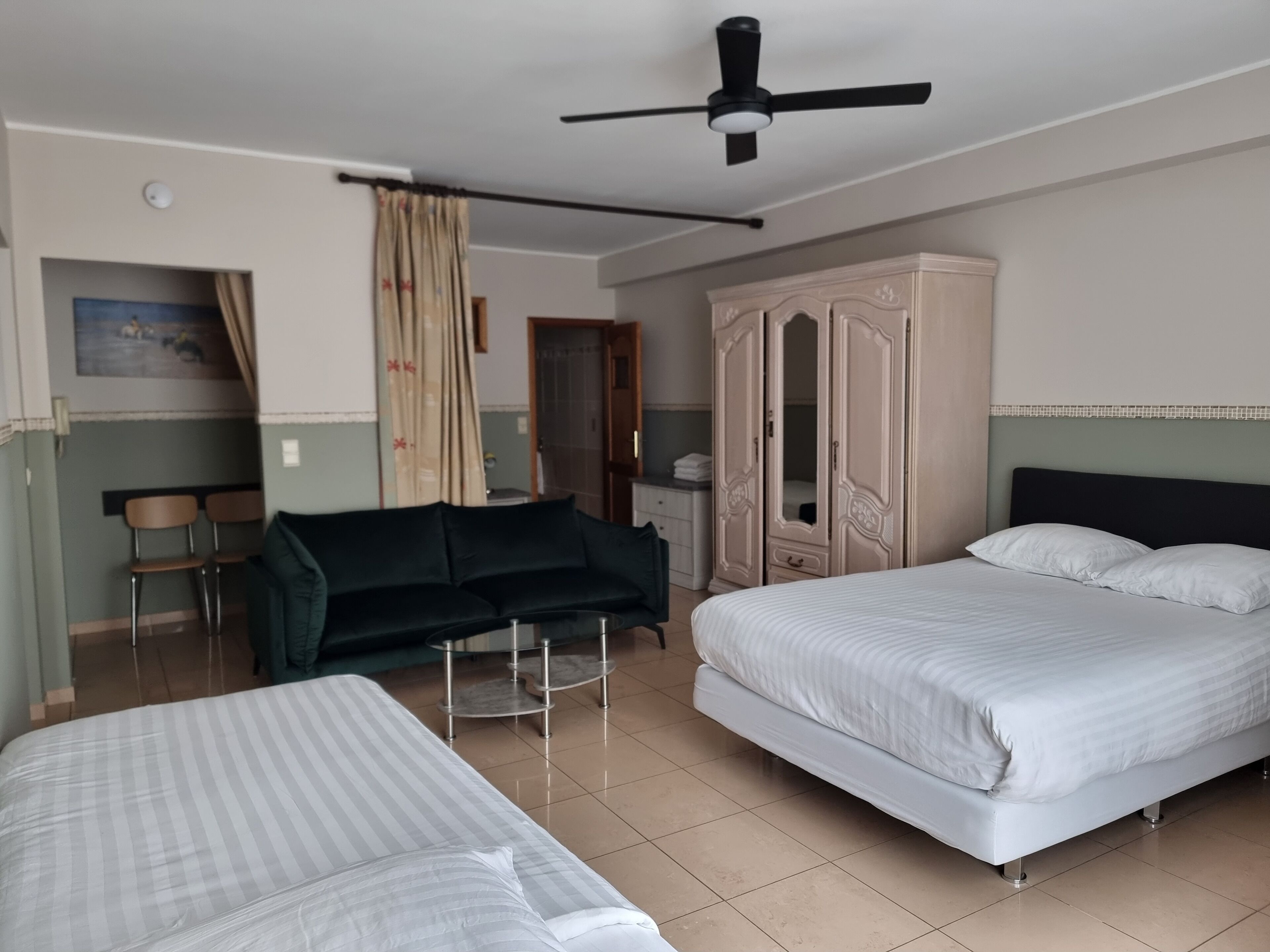 Een hotelkamer met twee bedden, een bank, een garderobe en een plafondventilator.