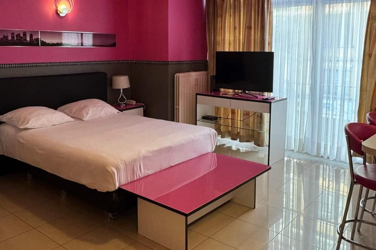 Habitación de hotel con cama, escritorio, silla, televisor y ventilador de techo.