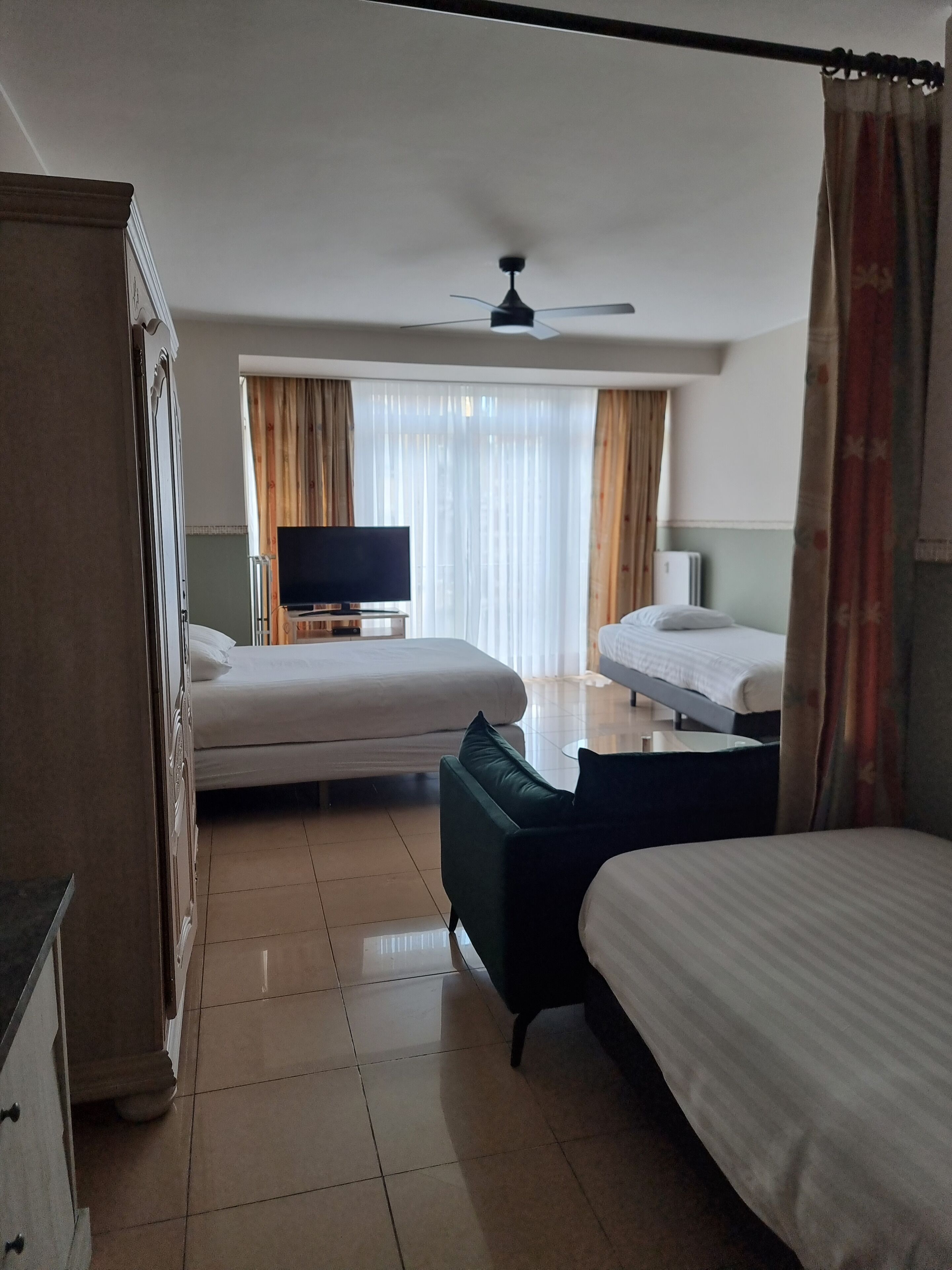 A hotel room with two beds, a TV, a ceiling fan, and a wardrobe.