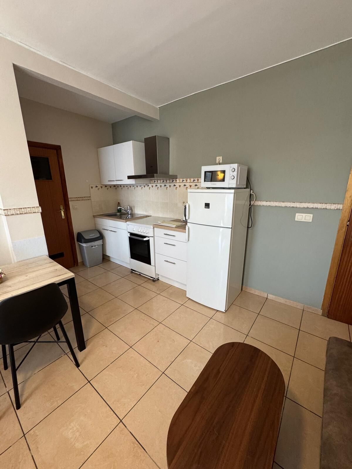 A compact kitchen with white appliances, a tiled backsplash, and a small dining area with a table and chairs.
