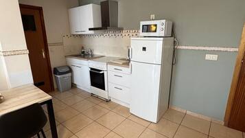 A compact kitchen with white appliances, a tiled backsplash, and a small dining area with a table and chairs.
