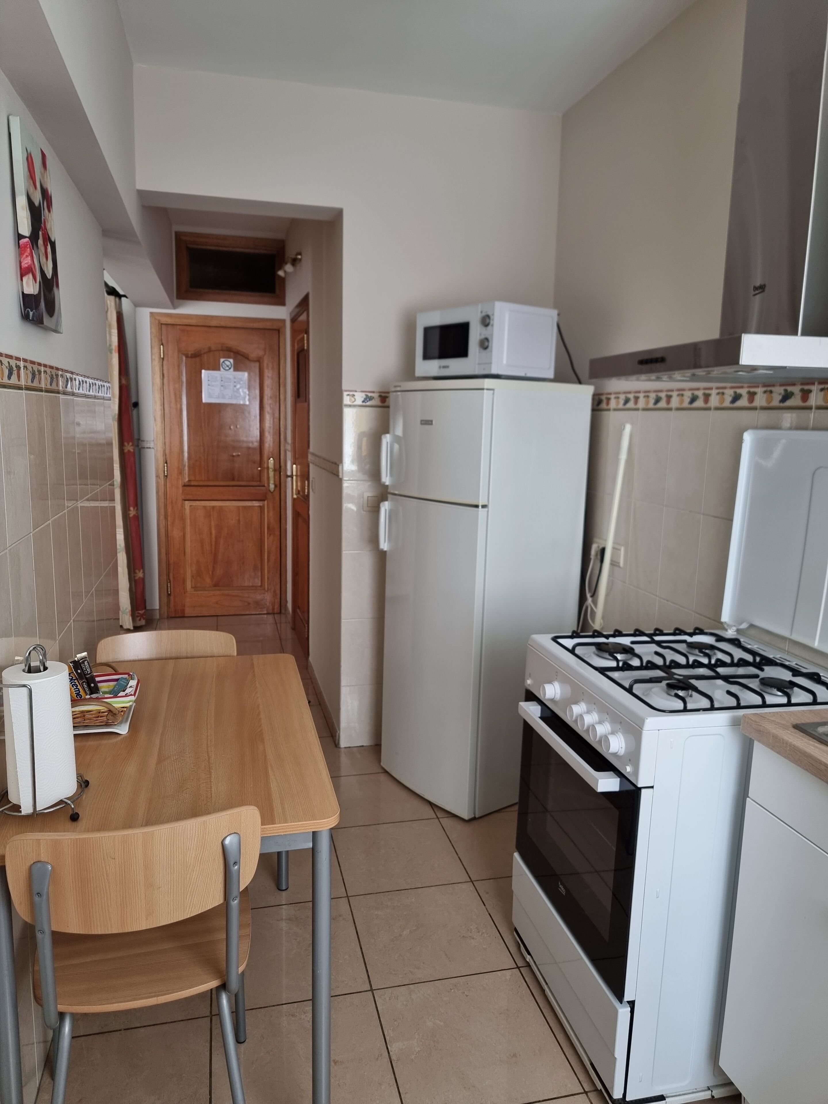 A kitchen with a wooden table, chairs, a refrigerator, a microwave, and a stove.