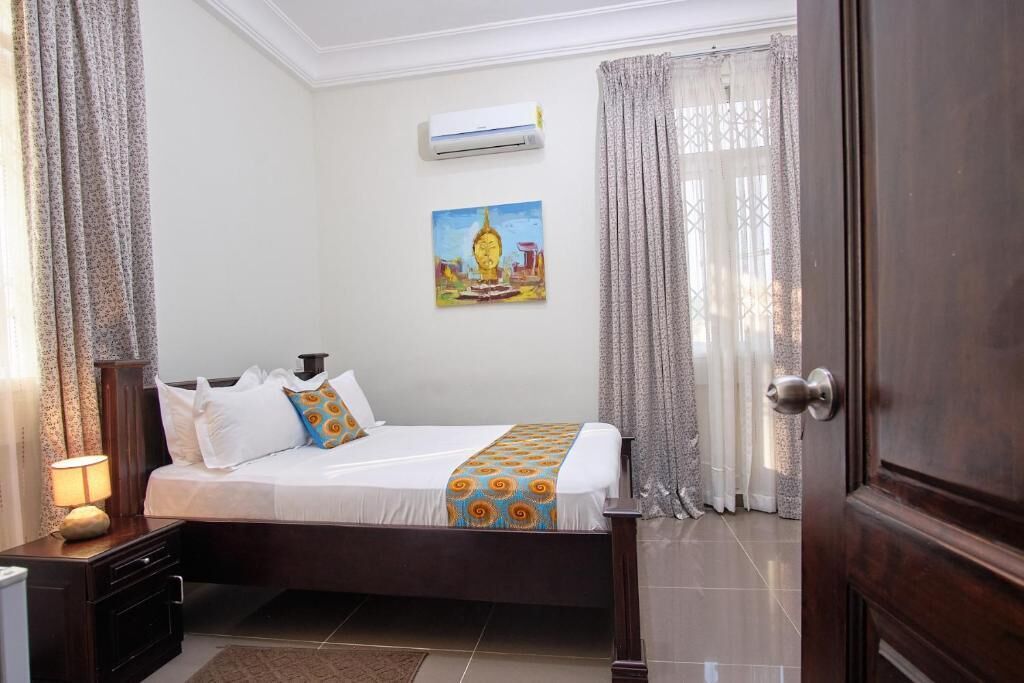 Habitación de hotel con cama, mesita de noche, unidad de aire acondicionado, un cuadro en la pared y una puerta.