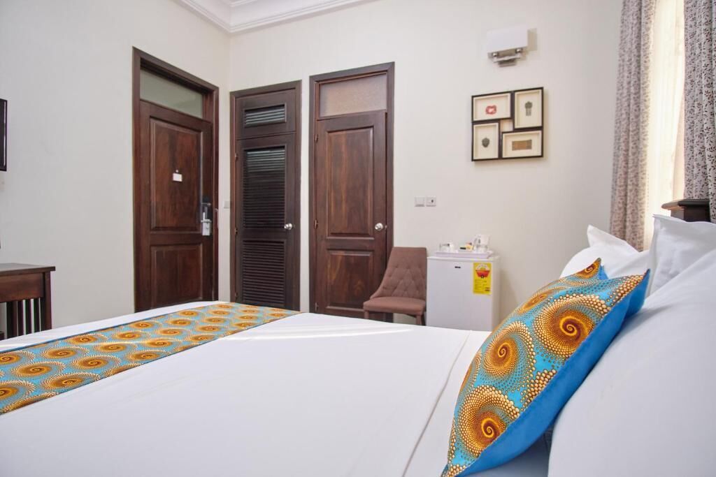 Habitación de hotel con cama, dos puertas, escritorio, silla, mesita y aire acondicionado de pared.