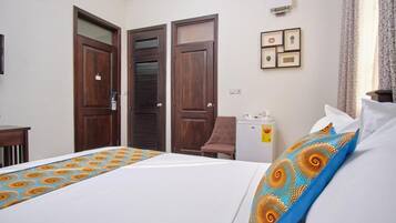 Habitación de hotel con cama, dos puertas, escritorio, silla, mesita y aire acondicionado de pared.