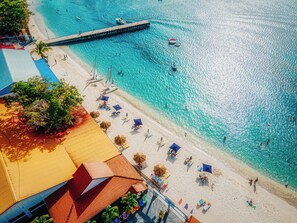Una playa con agua turquesa cristalina, un muelle de madera y sombrillas.