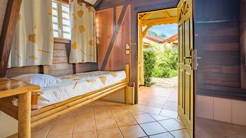Une pièce en bois avec un lit, une fenêtre avec des rideaux et une porte donnant sur l’extérieur.