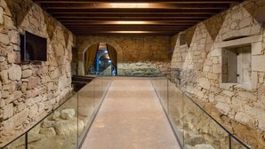 Un couloir aux murs de pierre, aux poutres en bois et à la rambarde en verre.