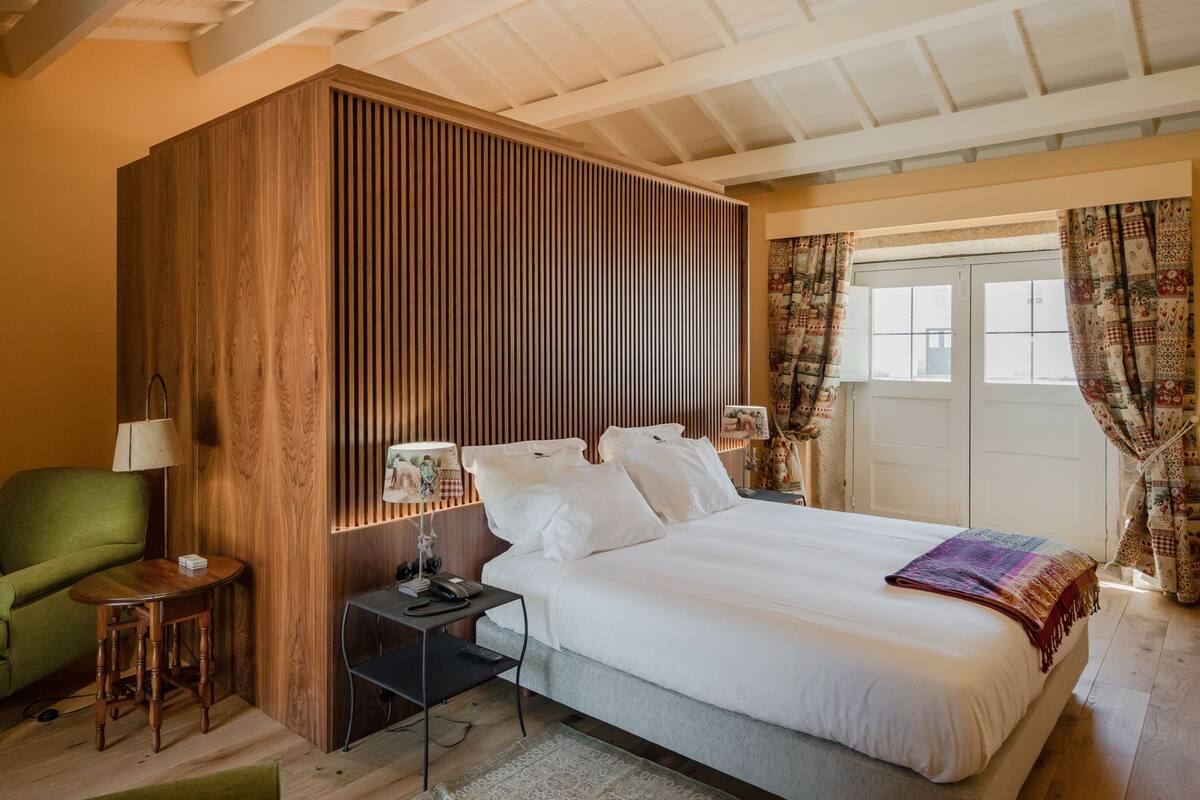 Un dormitorio ordenado con cama, mesitas de noche, lámpara y una silla.
