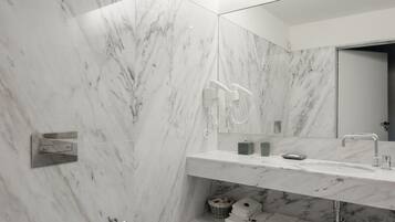 Un baño moderno con paredes de mármol, un espejo grande, un inodoro y un lavamanos con un toallero.