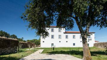 A white building with a red roof, surrounded by greenery and a stone wall.