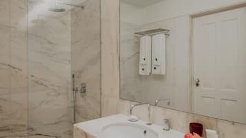 A modern bathroom with a glass-enclosed shower, a large mirror, and a marble countertop with two sinks.