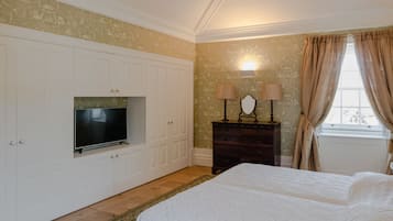 Un dormitorio con cama, televisor, cómoda y ventana con cortinas.