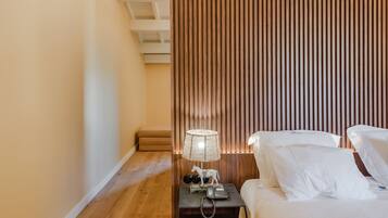 Une chambre d’hôtel avec un plancher en bois, un lit avec du linge de maison blanc, une table de chevet avec une lampe et une cloison en bois à lattes.