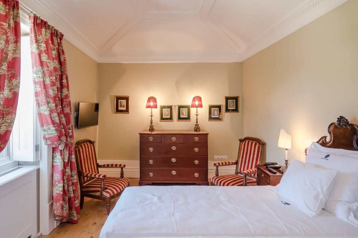 Una habitación de hotel con una cama grande, dos sillas, un tocador y un televisor en la pared.