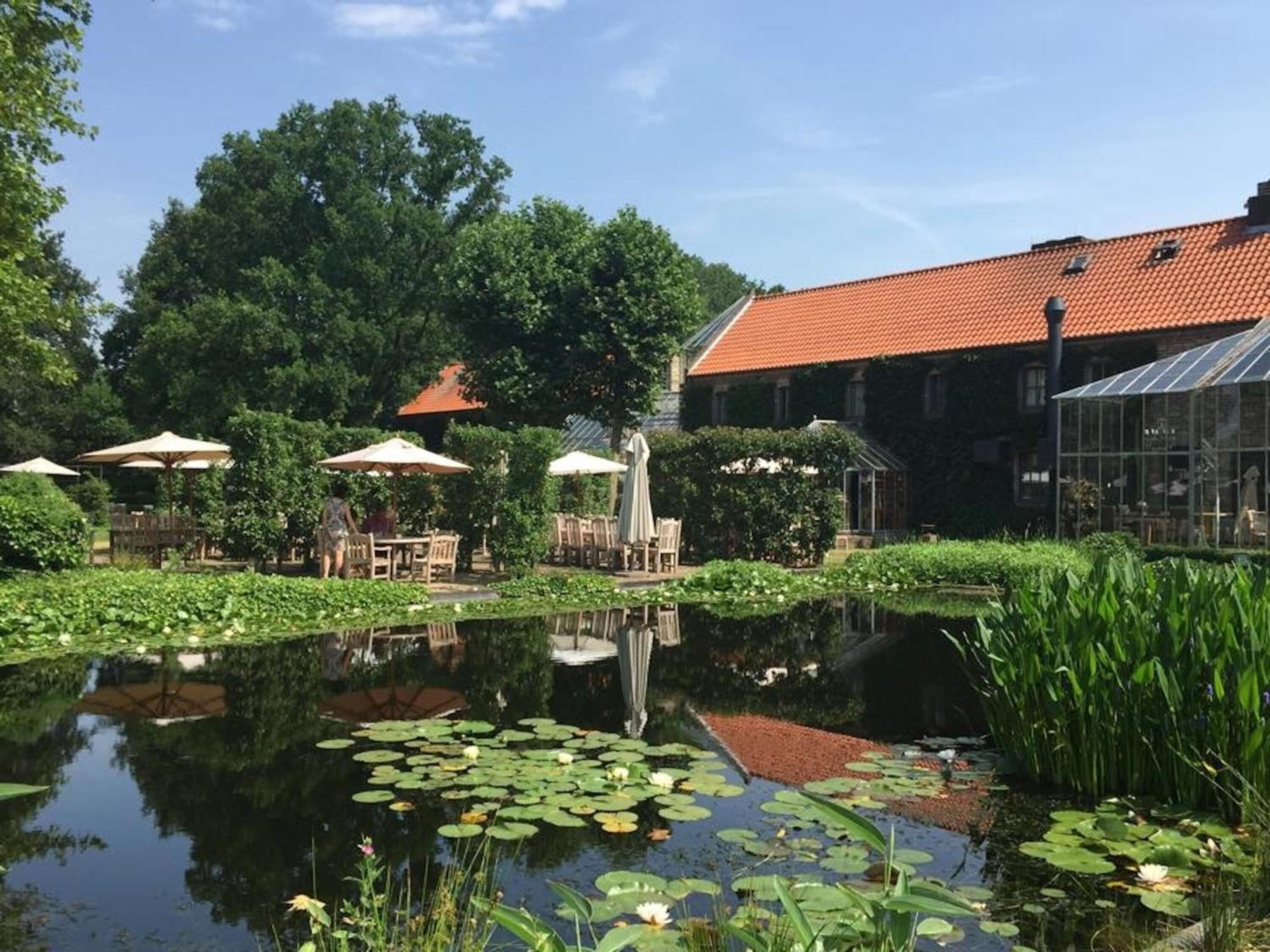 A serene garden with a pond, outdoor seating, and a building with a red roof.