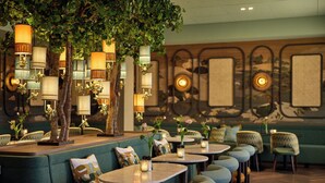 Een restaurant met groen bekleden zitplaatsen, ronde tafels, hanglampen en een muurschildering.