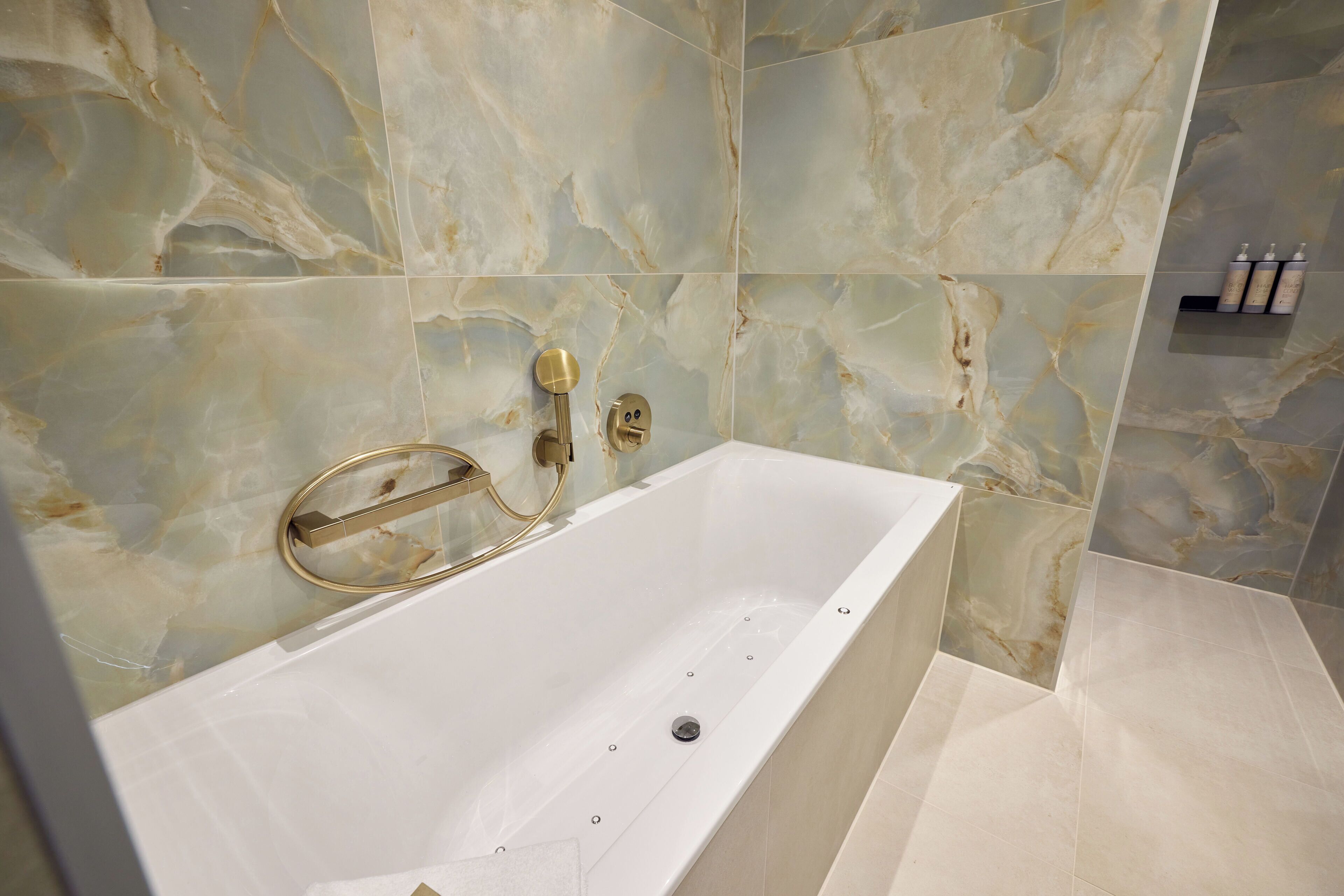 Een moderne badkamer met een marmeren wand, een witte badkuip en een gouden kraan.
