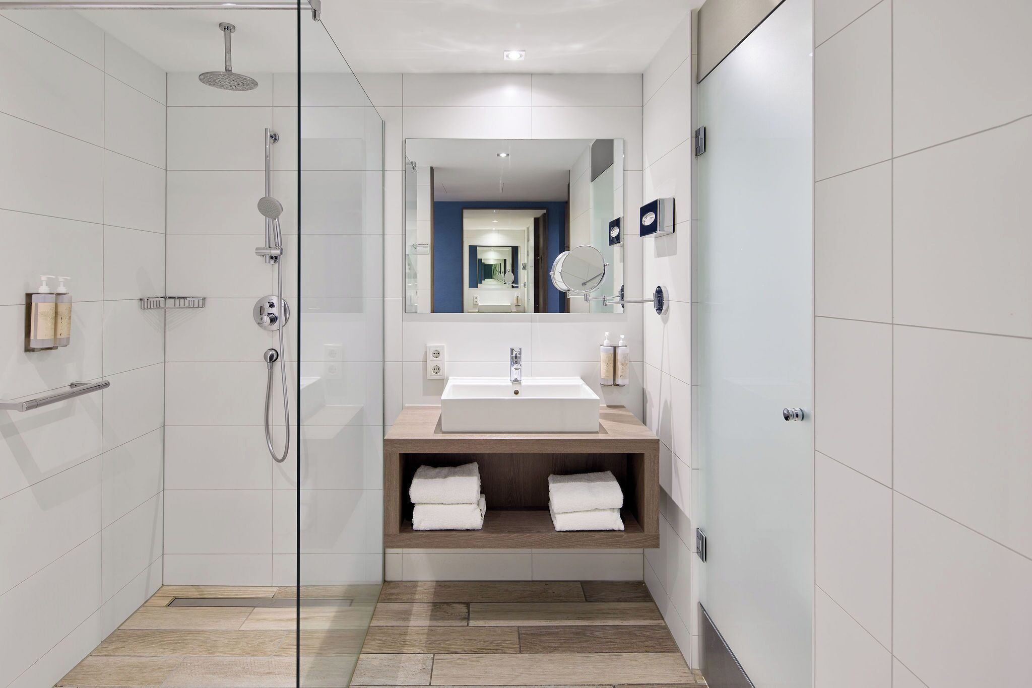 A modern bathroom with a glass-enclosed shower, a sink with a mirror, and a wooden vanity.