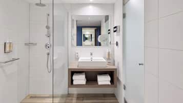 A modern bathroom with a glass-enclosed shower, a sink with a mirror, and a wooden vanity.