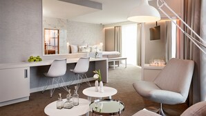 Una camera d'hotel moderna con zona pranzo, angolo salotto con lampada e vista sulla città.
