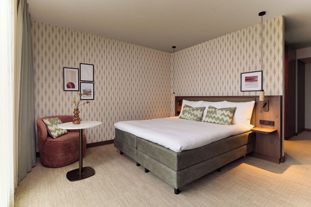 A hotel room with a large bed, a small round table, a sofa, and a wall with patterned wallpaper.