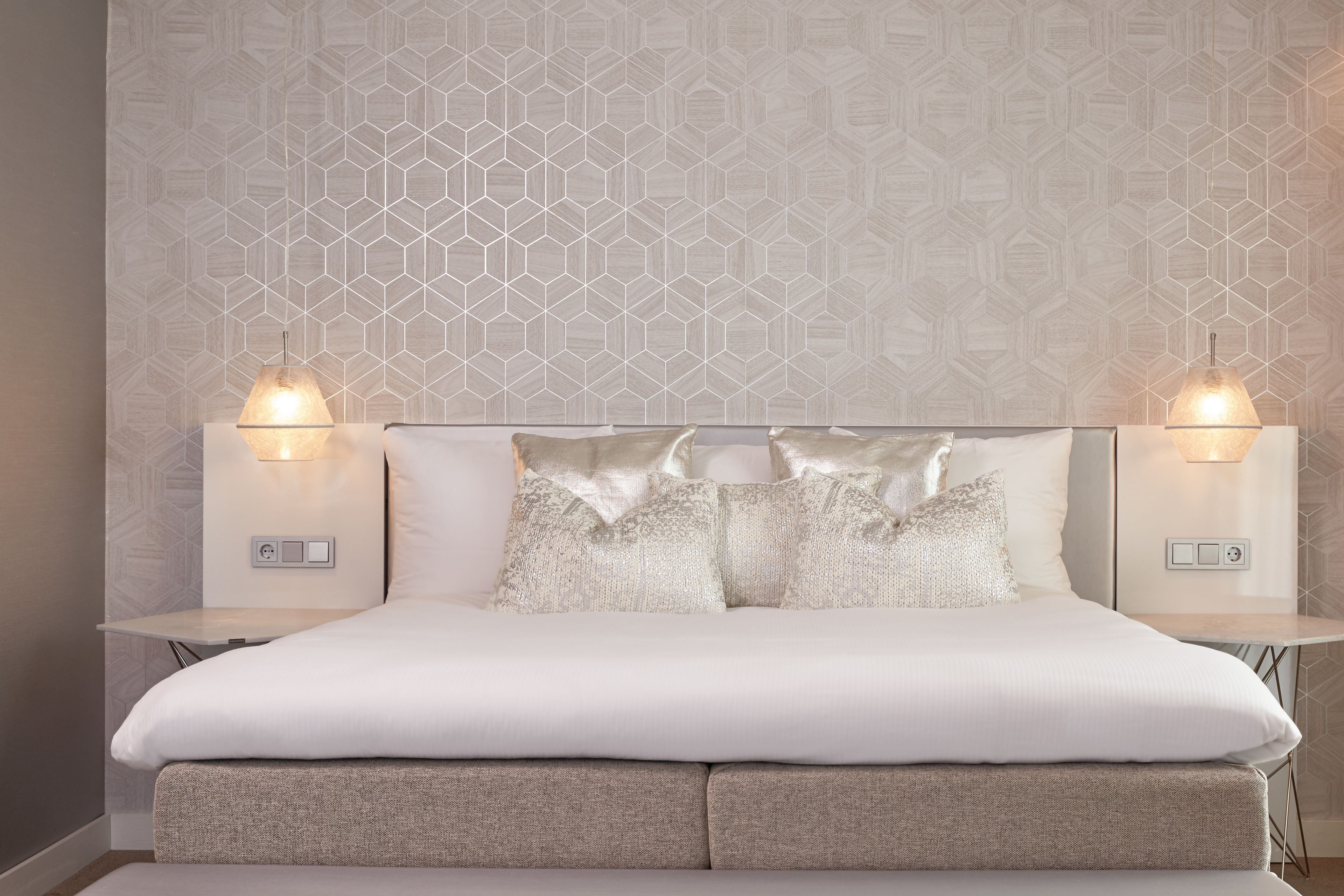 Un dormitorio con una cama grande, dos lámparas de noche y una pared con estampado geométrico.
