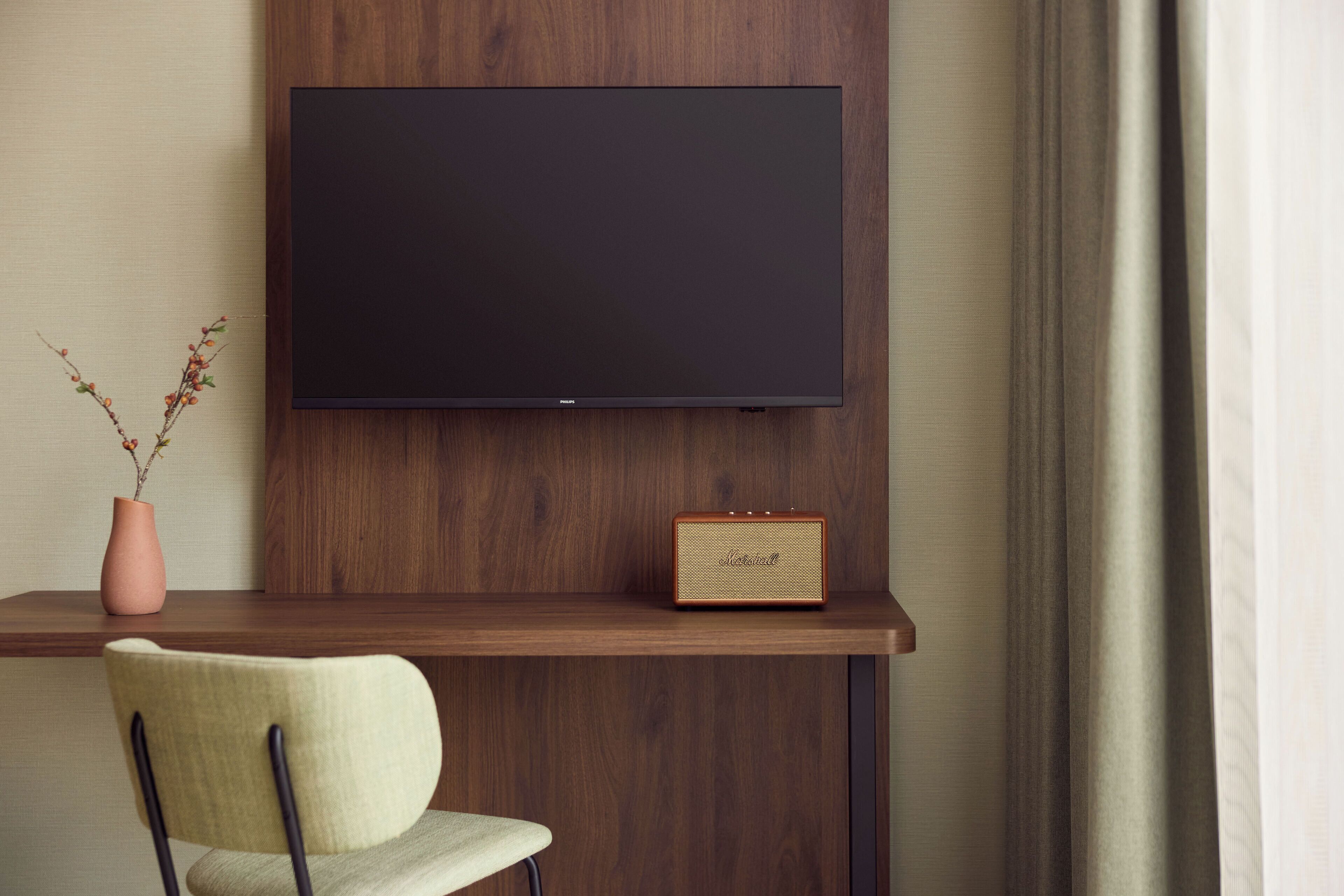 A modern room with a mounted flat-screen TV, a vintage radio, a vase with dried branches, and a chair.