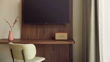 A modern room with a mounted flat-screen TV, a vintage radio, a vase with dried branches, and a chair.
