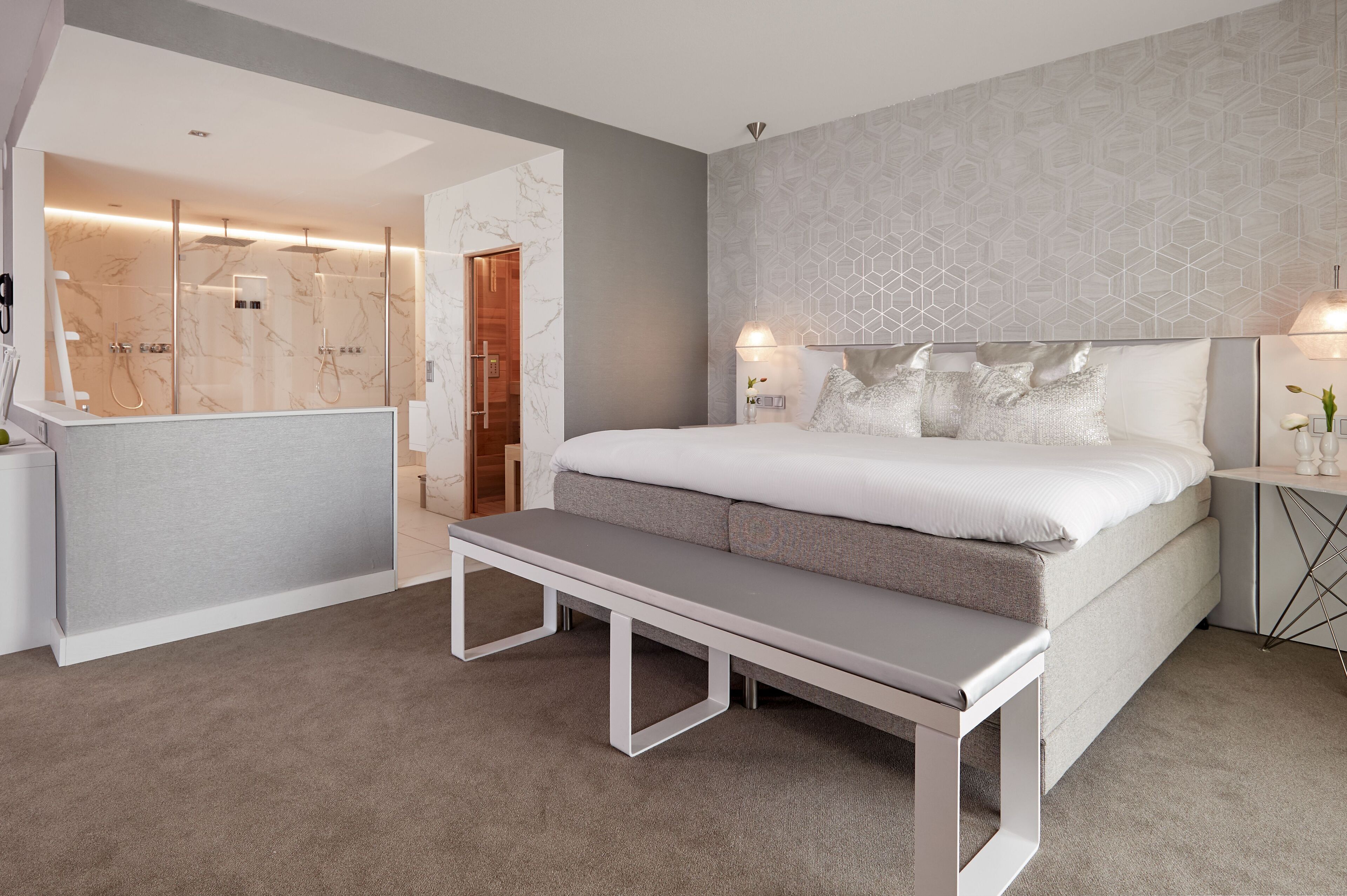 A modern bedroom with a large bed, a bench, a bedside table, and a shower area.