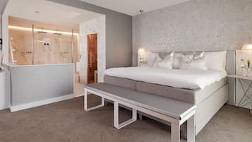 A modern bedroom with a large bed, a bench, a bedside table, and a shower area.