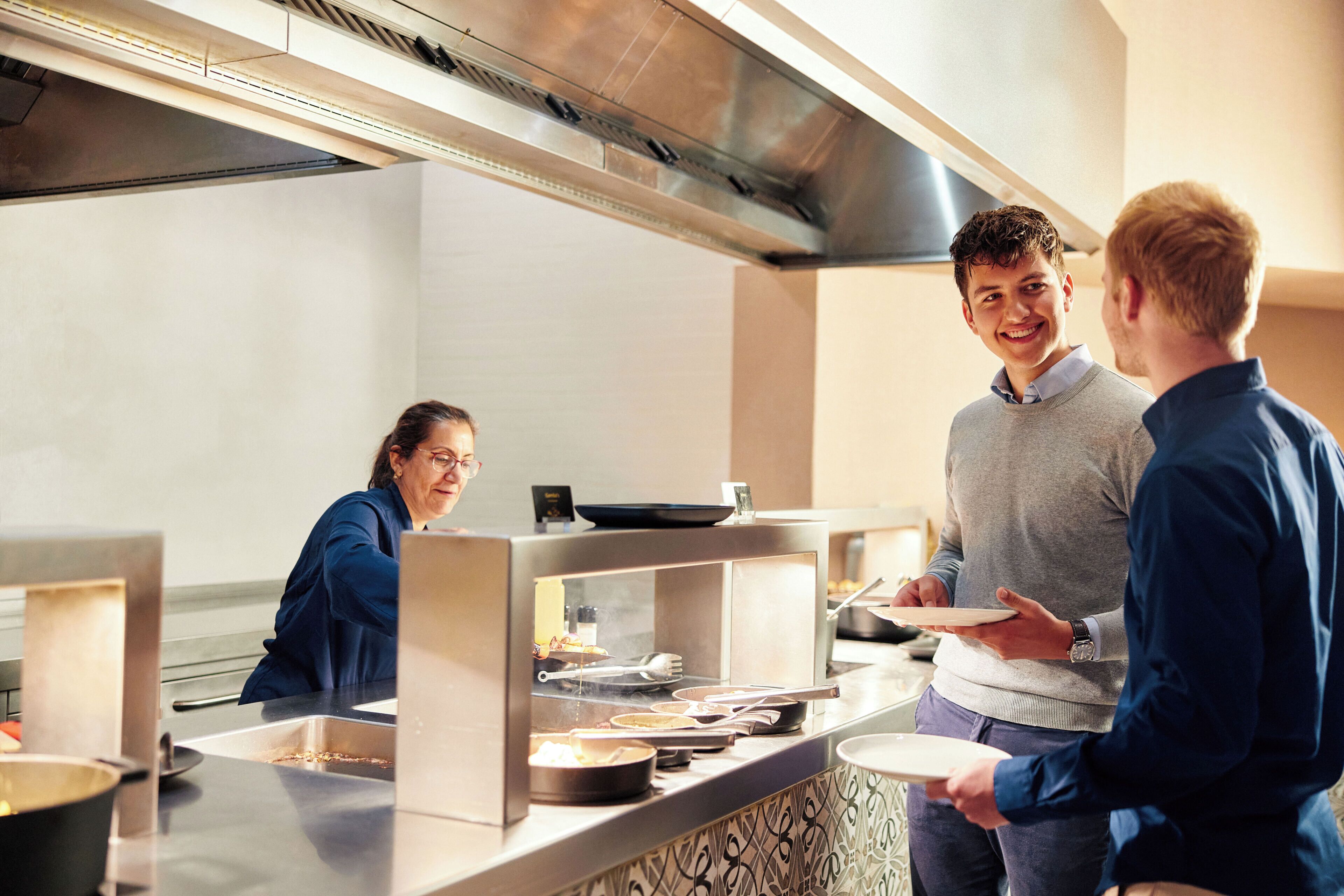 A kitchen area with stainless steel appliances, a buffet counter, and a person serving food.