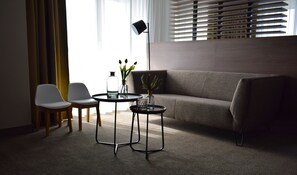 Ein modernes Wohnzimmer mit einem grauen Sofa, zwei weißen Stühlen, einem kleinen runden Tisch mit einer Lampe und zwei Vasen mit Pflanzen.