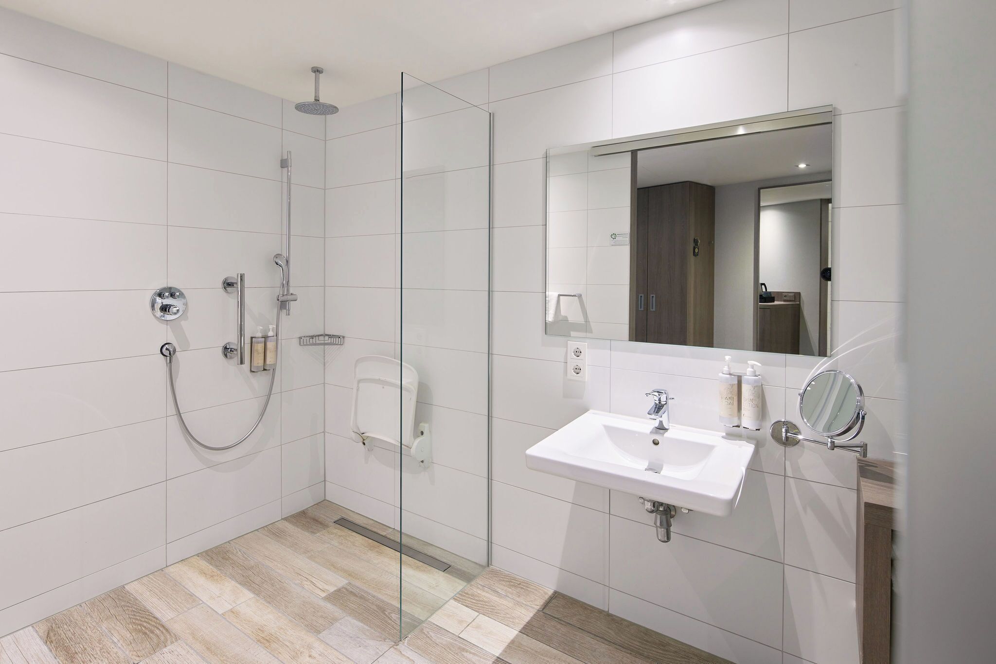 A modern bathroom with a glass shower enclosure, a white sink with a mirror, and a wooden floor.