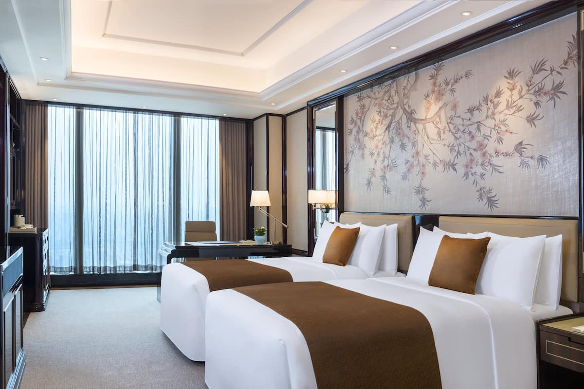Ein Hotelzimmer mit einem großen Bett, einem Schreibtisch, einem Stuhl und einem großen Fenster mit Vorhängen.