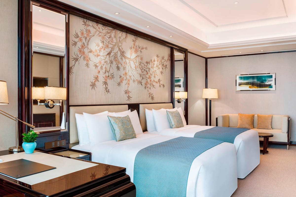 Ein Hotelzimmer mit zwei Betten, einem Sofa, einem Schreibtisch und einem großen Spiegel.