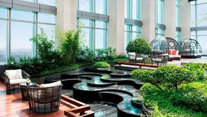 Un jardín interior moderno con zonas de estar, fuentes de agua y amplios ventanales.
