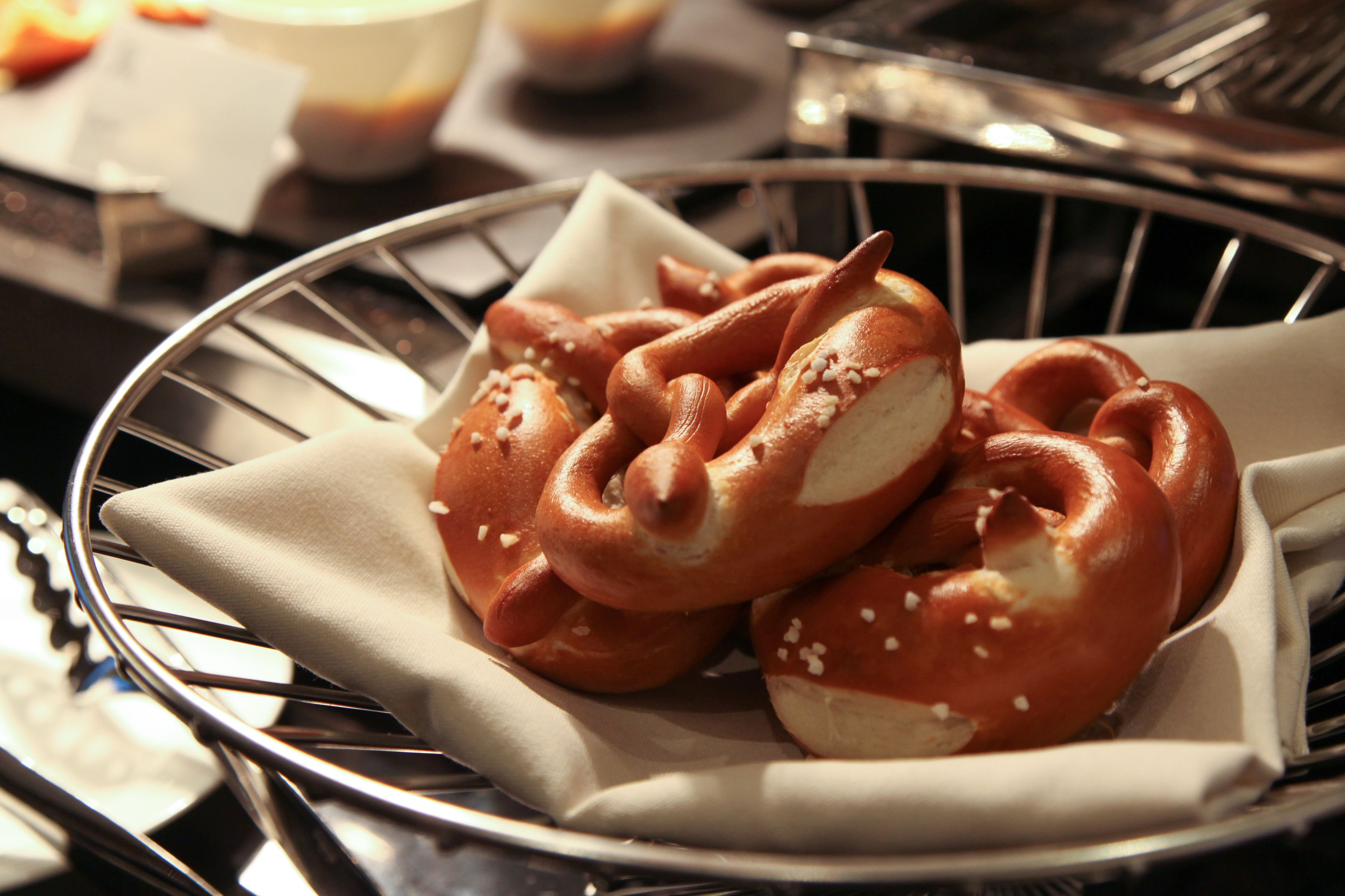 A metal basket containing pretzels with sesame seeds, placed on a table.