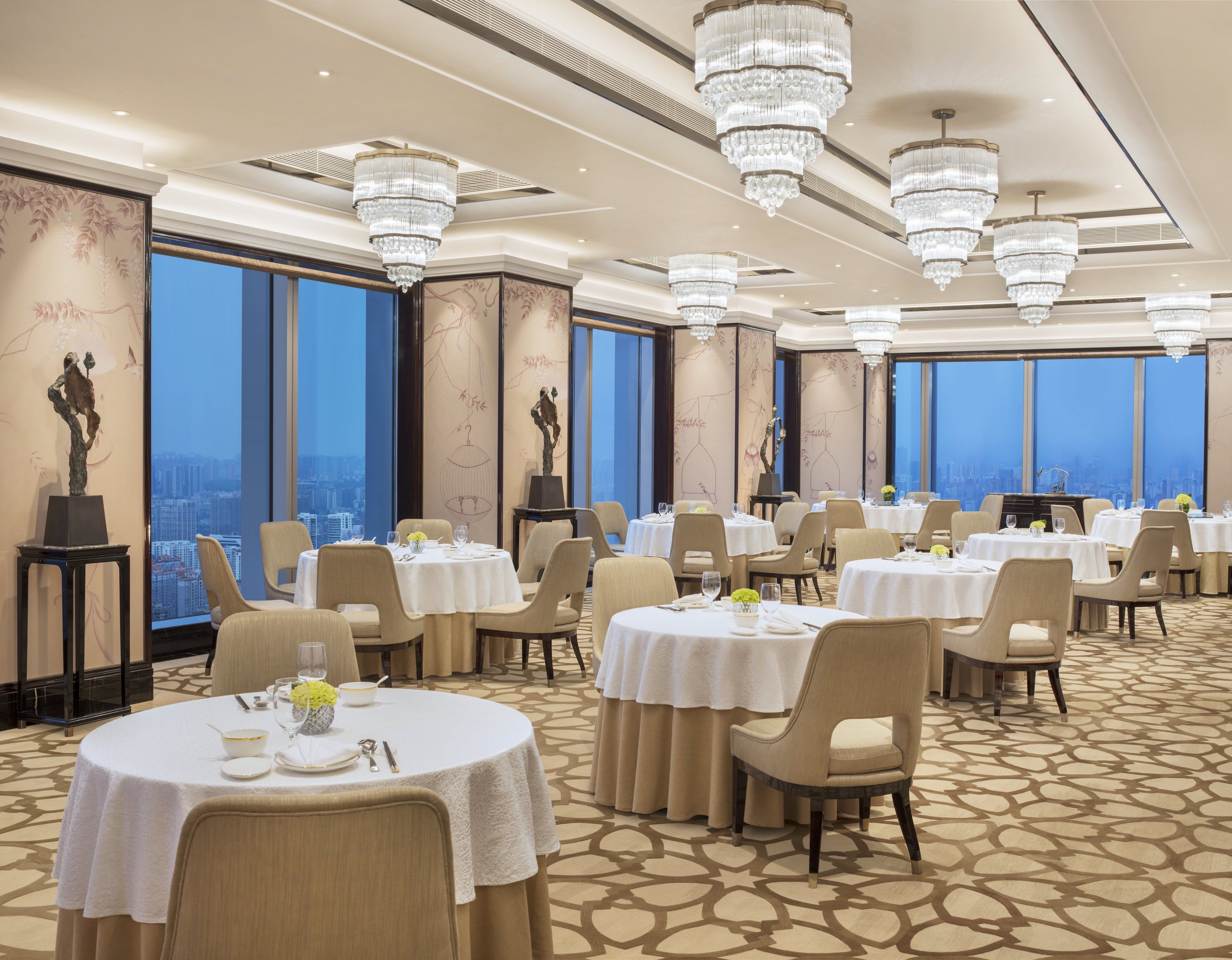 A dining area with round tables, chairs, and chandeliers.
